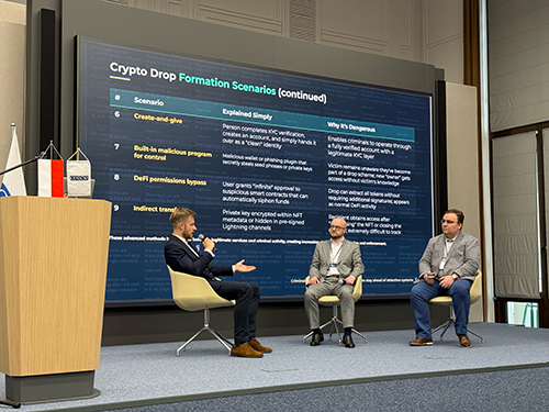 Three men sit on a stage in front of a large screen displaying a presentation about Crypto Drop Formation Scenarios. Two men sit on the right; one man on the left gestures while speaking into a microphone.
