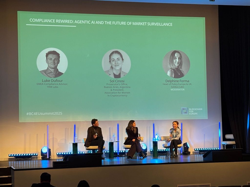 Three panelists sit on stage with microphones under a large screen displaying their photos, names, and titles, discussing Compliance Rewired: Agentic AI and the Future of Market Surveillance at a conference.